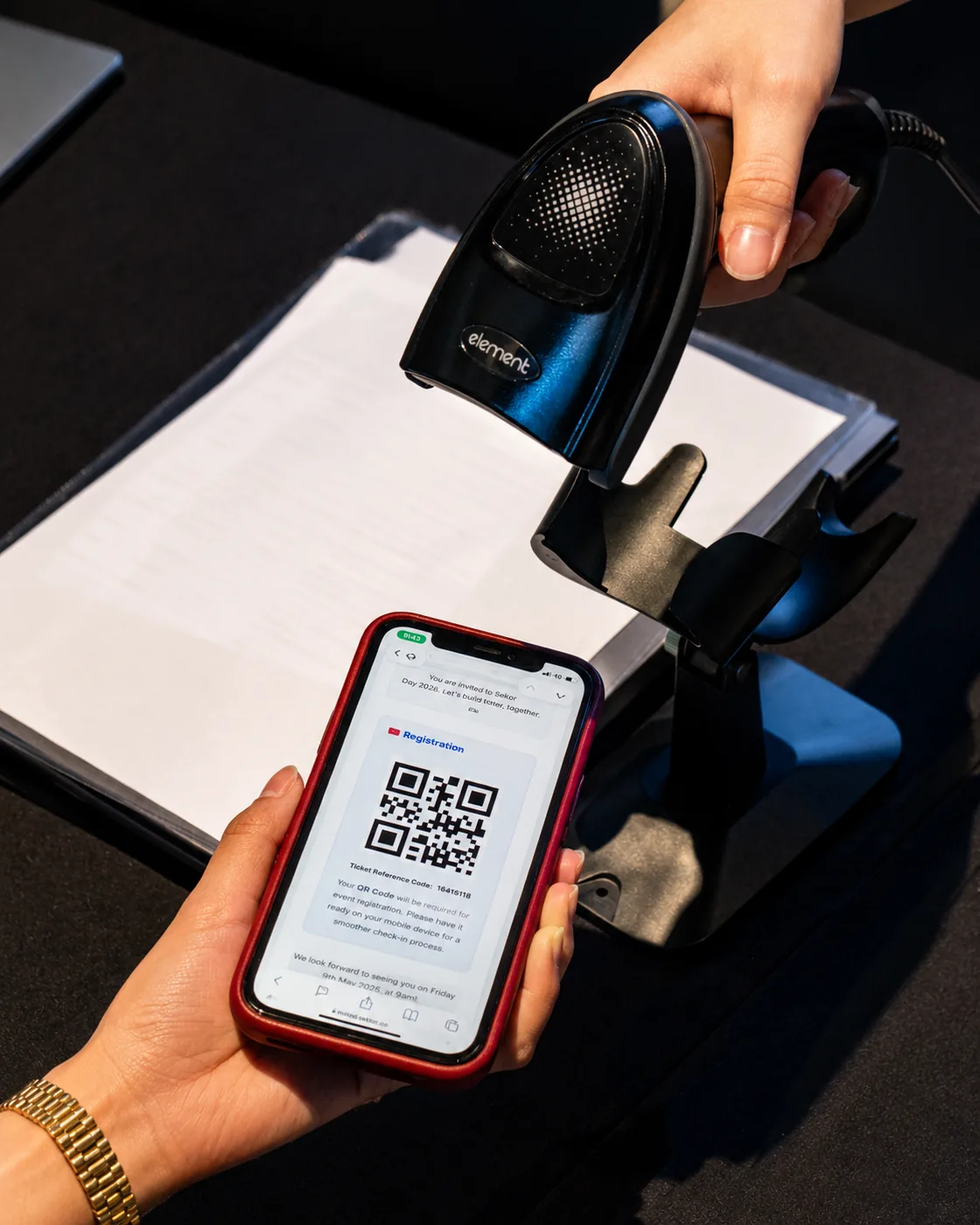 Handheld QR barcode scanner reading a QR code from an attendee's phone