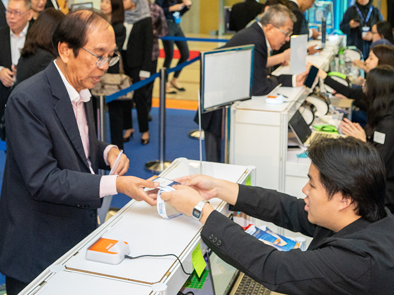 Check-in crew handing a printed badge and lanyard to a guest at a corporate event registration counter